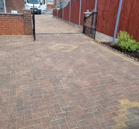 Brick paved driveway with black post and metal gate, red fence