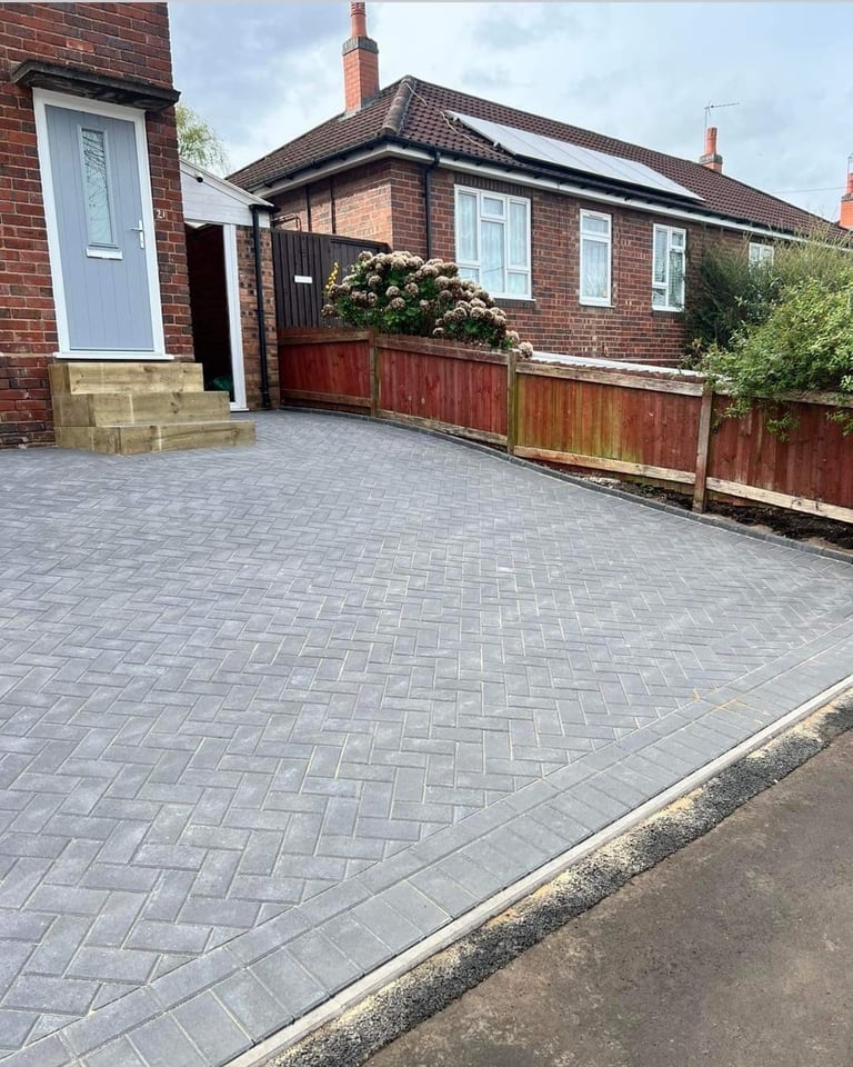 Brick bungalow with newly paved herringbone driveway, red wooden gate, and white entrance door