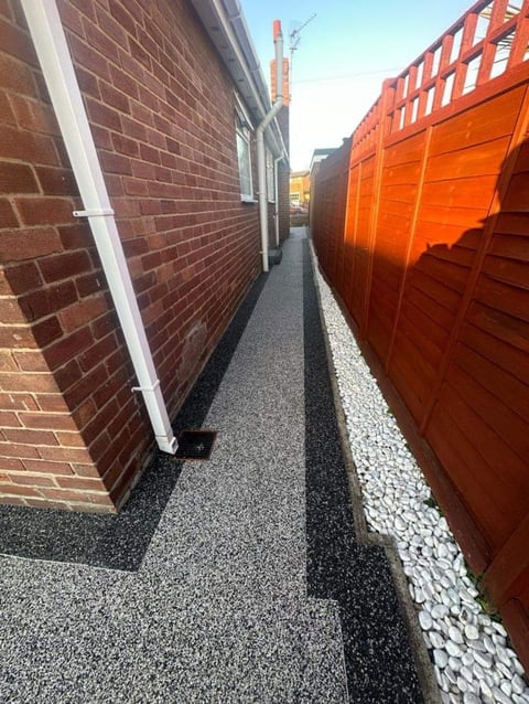 Narrow alleyway between a brick building and red wooden fence with gravel pathway