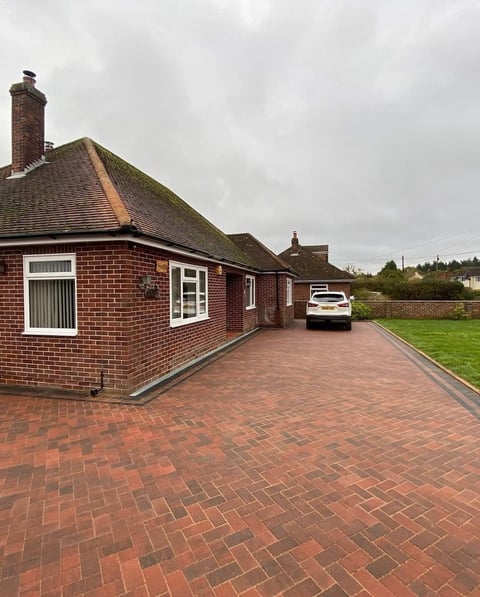 Red brick bungalow with driveway, parked white car, and green lawn