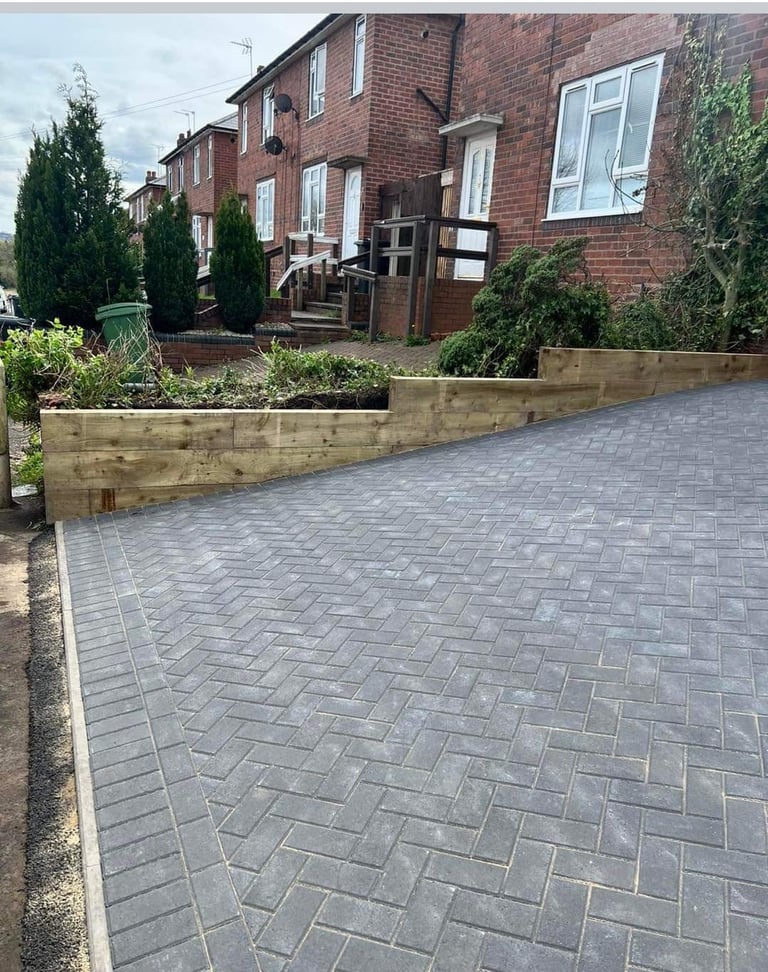 Newly installed gray herringbone paved driveway in front of a brick residential house with landscaped garden beds