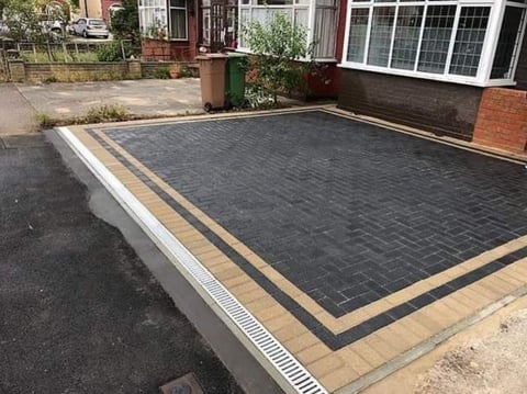 Newly laid black herringbone brick driveway with tan border in residential courtyard
