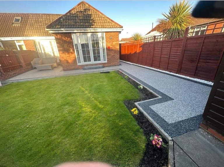 Modern brick home with manicured lawn, gravel patio, and dark wood fence in sunny backyard