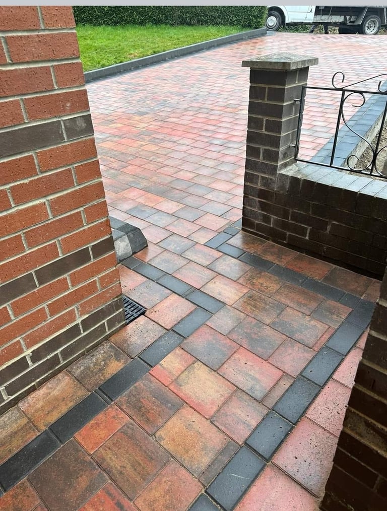 Brick driveway with dark border trim and chimney pillars, extending toward a parked truck and green lawn in background