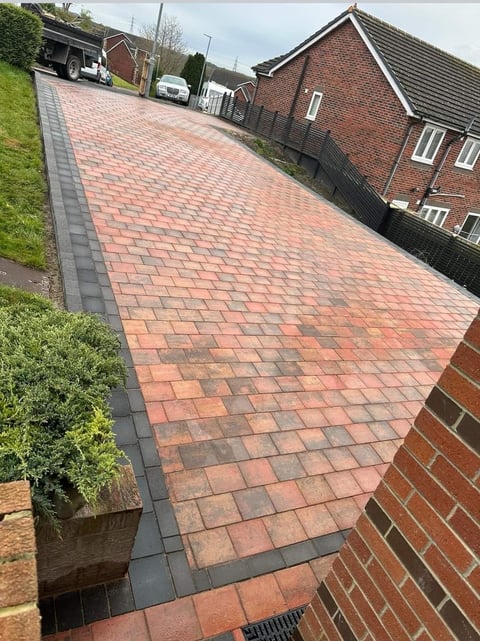 Newly paved brick driveway with geometric pattern leading to brick house